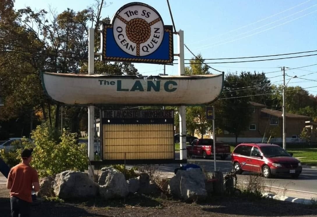 A street‑side view of The LANC’s canoe‑shaped sign with “The SS Ocean Queen” mounted above it, photographed along Bridgeport Road in front of The Lancaster Smokehouse.
